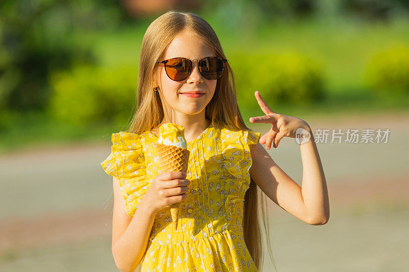 戴着墨镜，穿黄色裙子的金发女孩在吃冰淇淋。夏天的生活方式。童年