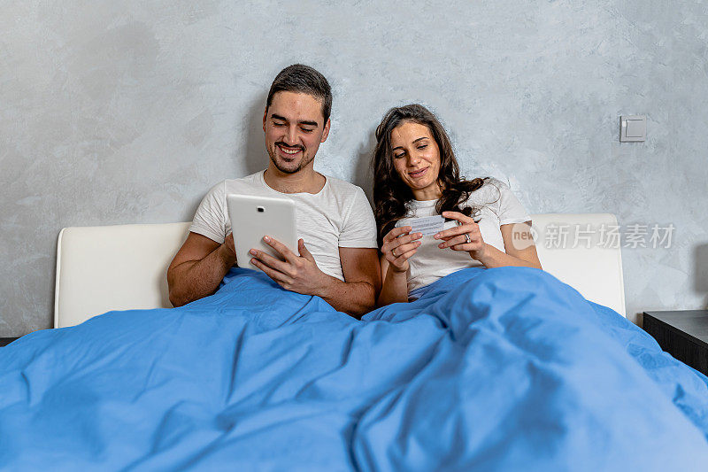 夫妇在舒适的床上用平板电脑和信用卡享受购物