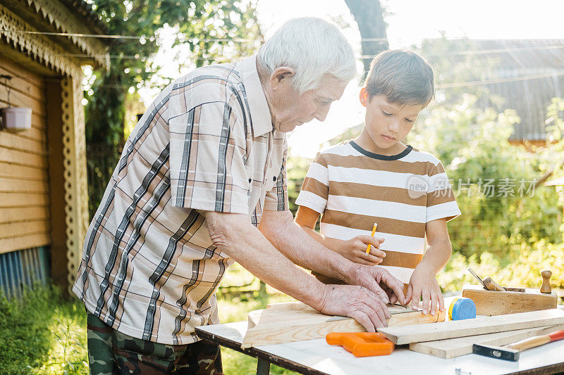 一位老人和一个男孩在房子的后院做木工活。孙子帮爷爷做。