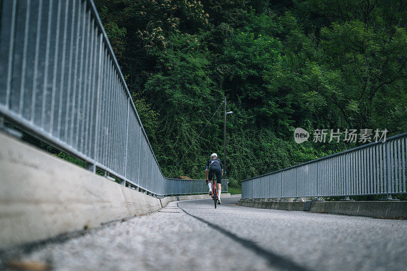 男子公路骑自行车在乡村公路在早上的看法