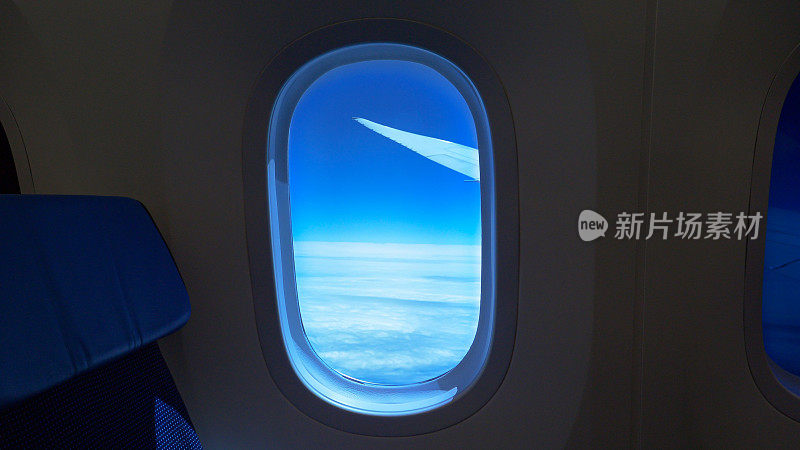 透过飞机窗户看到飞机机翼和云层之上的蓝天