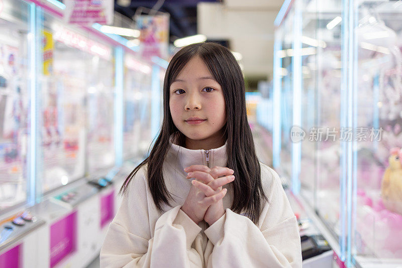 十几岁的女孩在游乐场的起重机游戏前祈祷成功