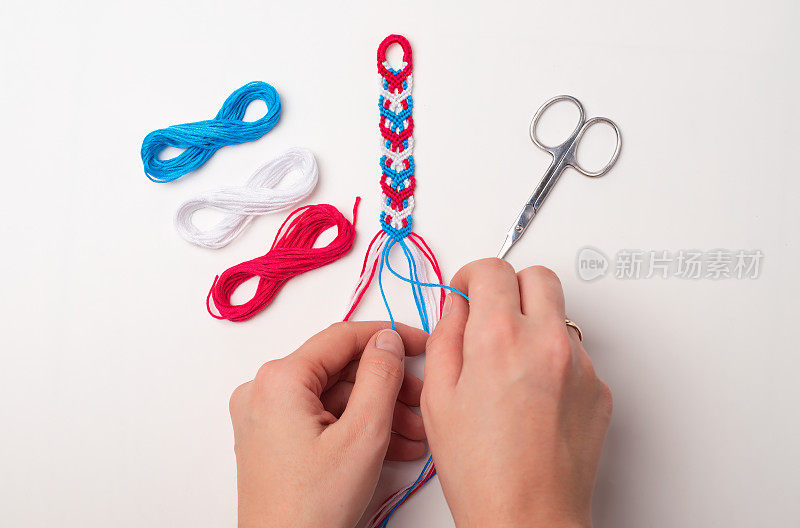 编织结DIY友谊手链的过程。女性的手。一步一步来。白色背景与复制空间，剪刀和线