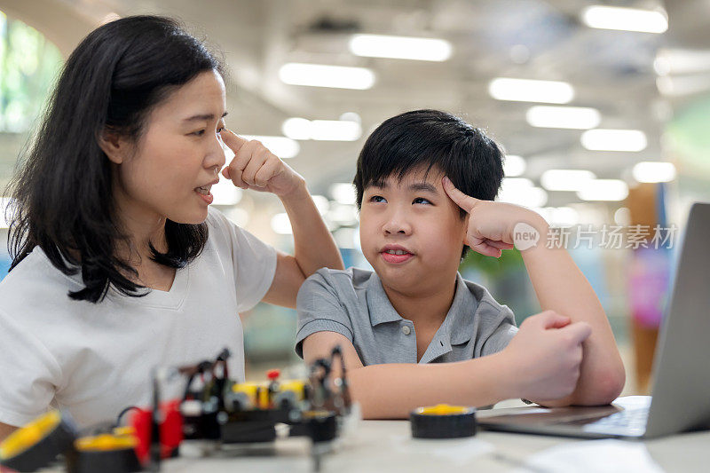 一名亚洲小学生正在一位专家老师的指导下学习如何组装机器人和使用编程语言。男孩很专注，很投入，按照老师的建议和指导来建造和编程机械臂。