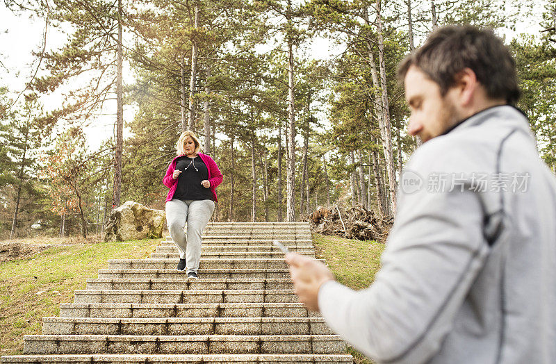 超重的女人跑下楼梯，私人教练在检查她的表现。肥胖人群户外锻炼，朋友、健身教练的支持。