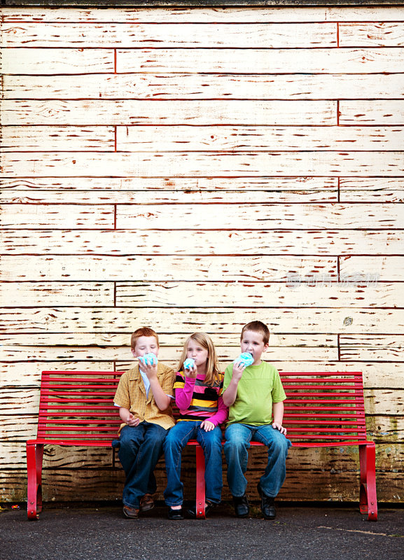 三个可爱的孩子在长凳上吃棉花糖