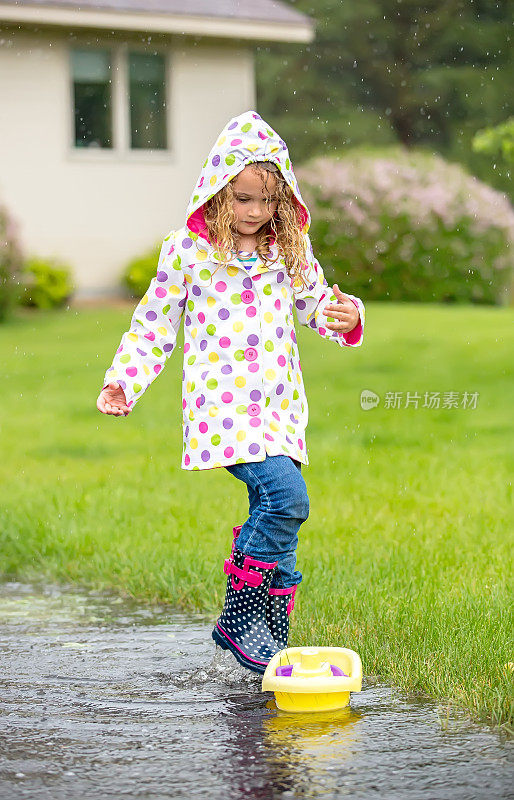 小女孩在雨坑里玩玩具船