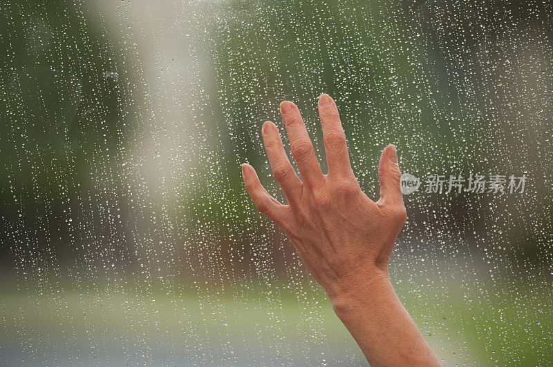 一只年老的手触着一扇满是雨滴的窗户