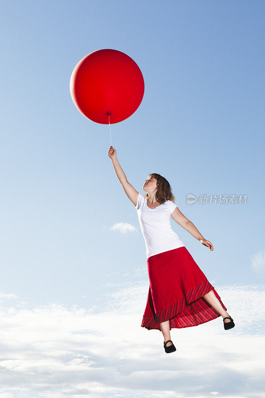 一个年轻的女人带着一个红色的气球飞过云层