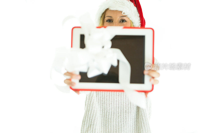 一名年轻女子戴着圣诞帽，手里拿着一份数码平板电脑礼物。