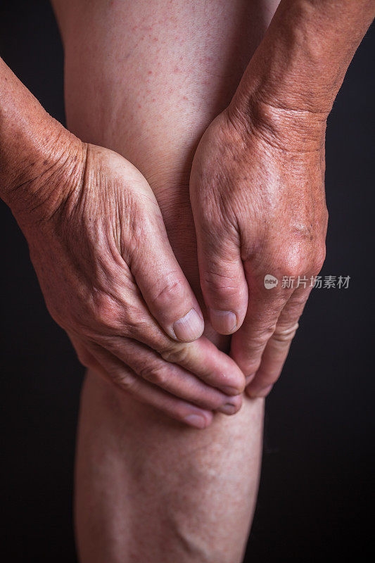 一个老人用黑色的背景抱着他的膝盖