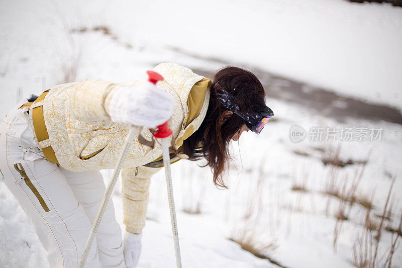 近景美丽的年轻女子在冬天的衣服站在一边，手拿木棍的背景雪山