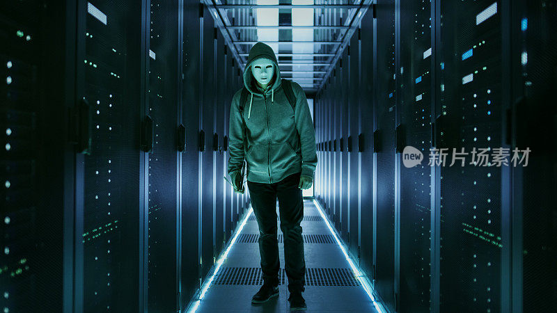 一个穿着帽衫的蒙面黑客站在数据中心，旁边是一排排机架服务器。