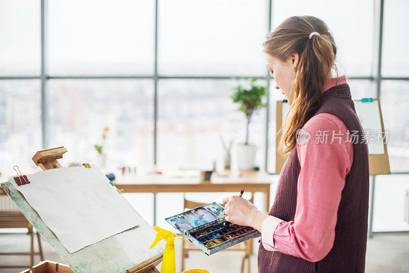 一个年轻女子画家的肖像用水彩调色板在纸上使用画架。