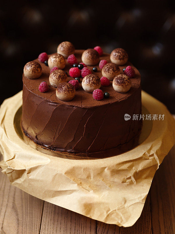 特写的巧克力蛋糕与覆盆子，黑醋栗，撒可可在棕色的木制背景。