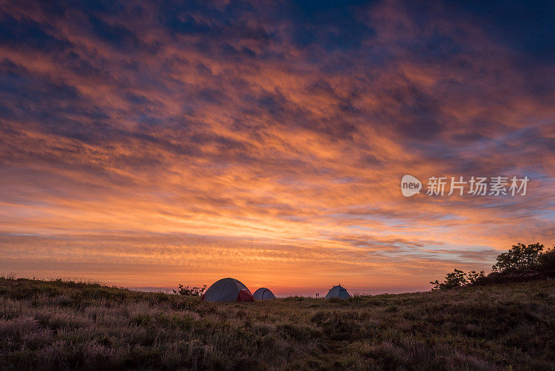 明亮的橙色云彩在三个帐篷上方闪烁