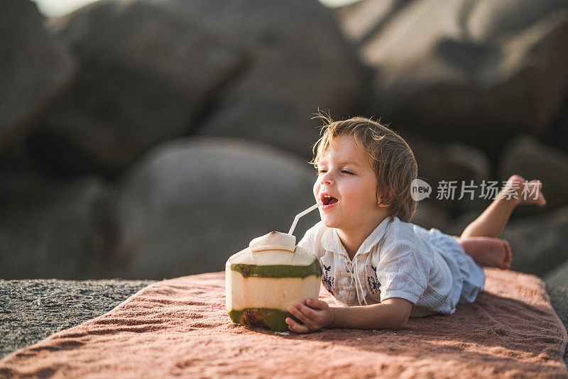 可爱的男孩躺在石头上喝着新鲜的椰子。