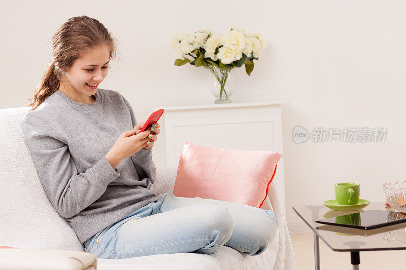 年轻女子微笑着躺在家里的沙发上，用智能手机在网上发短信