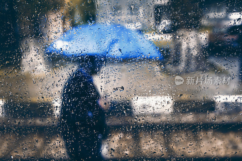 雨落在玻璃上，和拿着蓝伞的男人