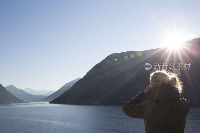 女人俯瞰湖面，看到太阳从山上升起。