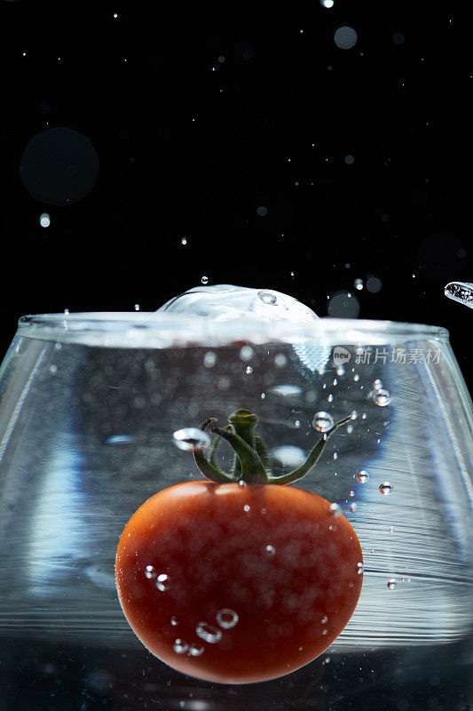 红色圆圆的迷你番茄掉进了玻璃杯的水里，溅起的水花是美丽的