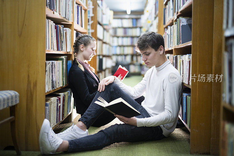 一对青少年情侣在图书馆闲逛，几个学生在图书馆看书。