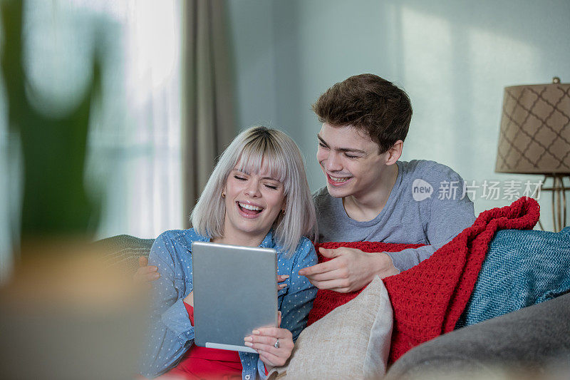 幸福的年轻夫妇微笑着一起在沙发上使用数码平板电脑