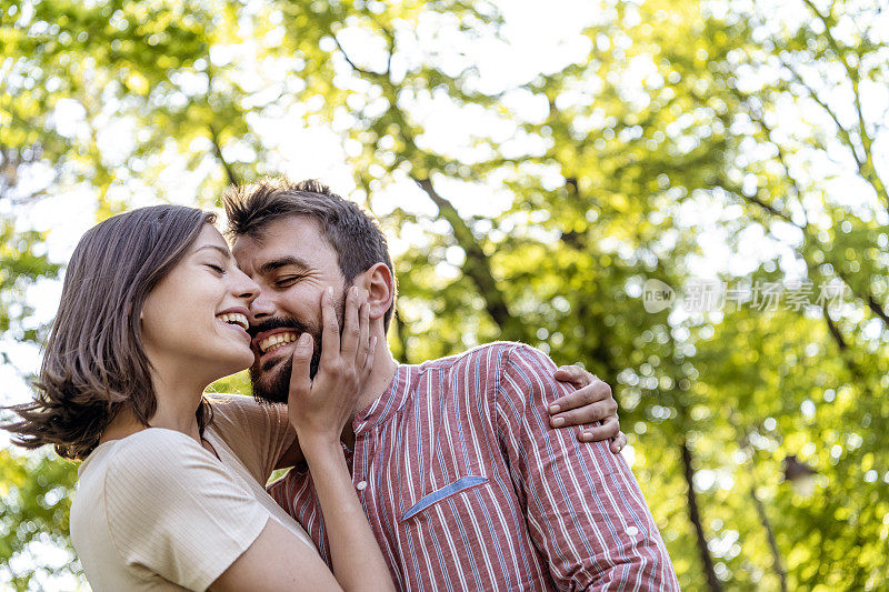 一对年轻夫妇正在公园里享受春天。他们在一起的时候，爱得更深。年轻的情侣在公园里微笑着拥抱。