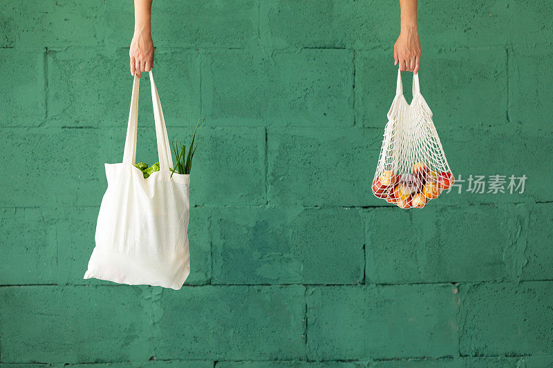 女性的手与购物棉网环保袋在绿色的背景。“零浪费”的概念