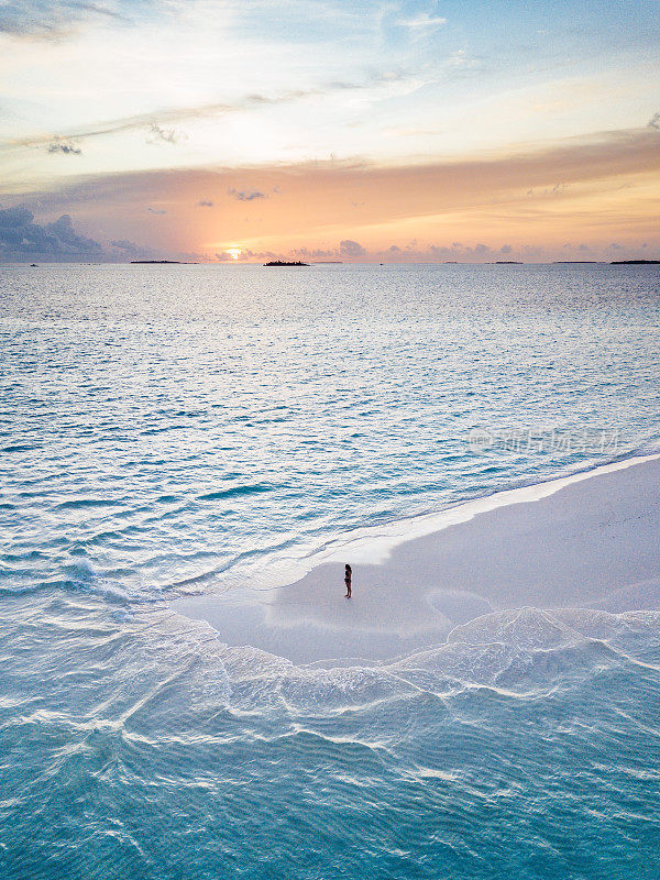 日落时分，年轻的成年女子站在马尔代夫碧绿的沙滩上