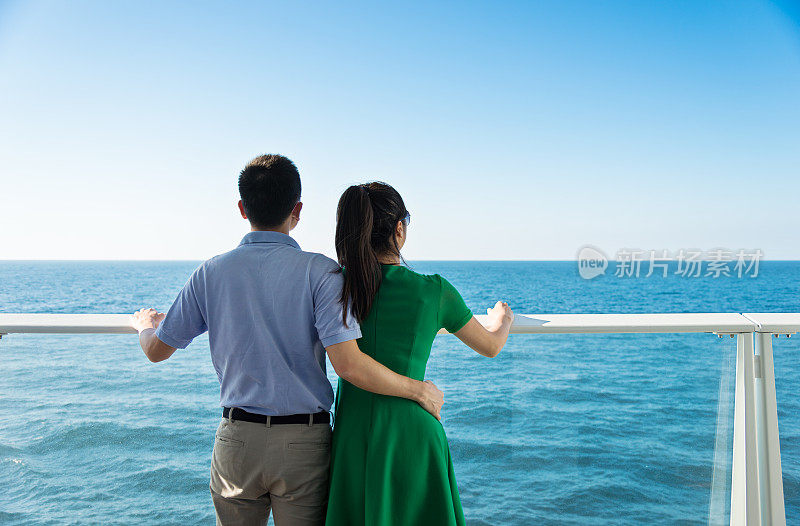 一对年轻夫妇在游轮上搂着胳膊欣赏风景