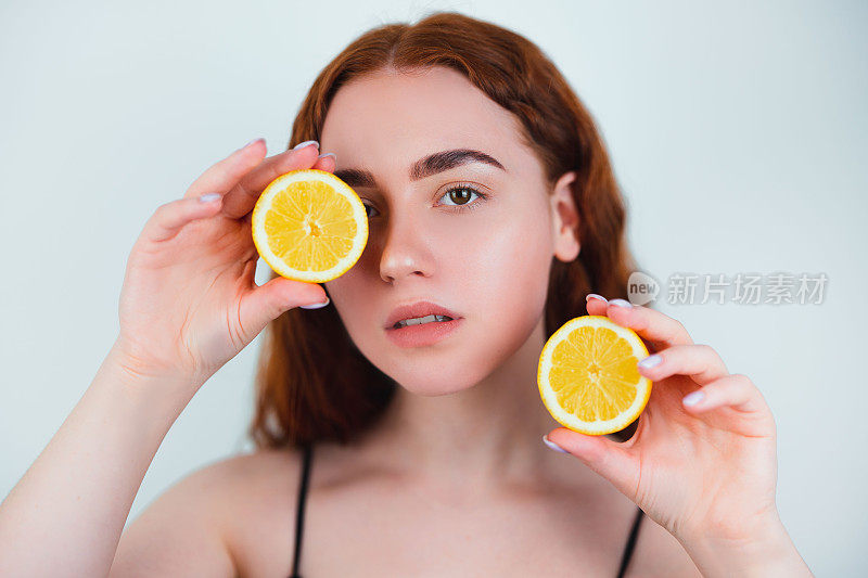 肖像的红发年轻女子站在孤立的白色背景持有一半的橙色在手中闭上她的眼睛与另一半，美丽肖像的概念