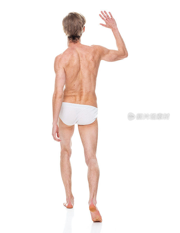 白人年轻男子穿着泳裤走在白色背景前