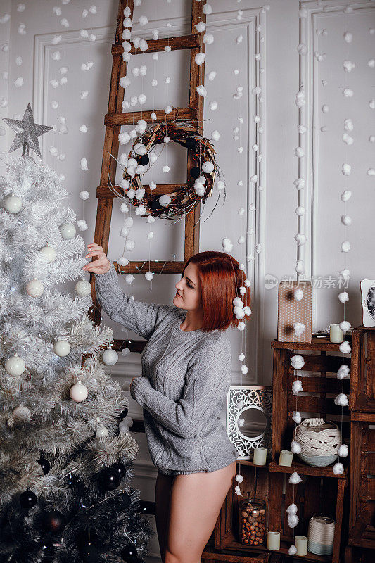 时尚室内照片美丽的年轻女子红头发和迷人的微笑，穿着舒适的针织羊毛衫，摆姿势与圣诞树和巧克力蛋糕与星号的礼物