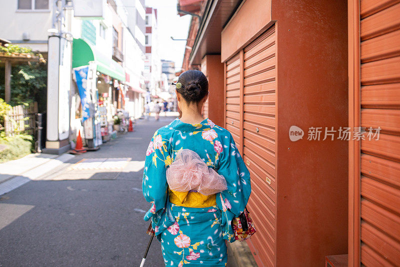 后视图的年轻女子在yukata行走在传统的日本村庄