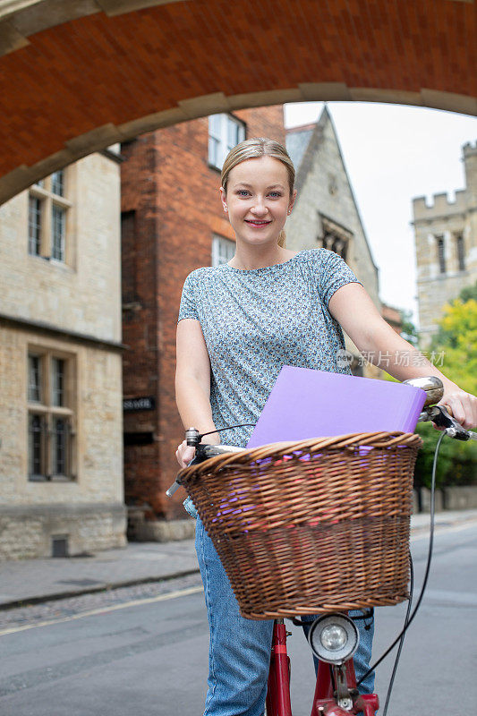 女学生在叹息桥旁骑着老式自行车绕着牛津大学大楼的肖像