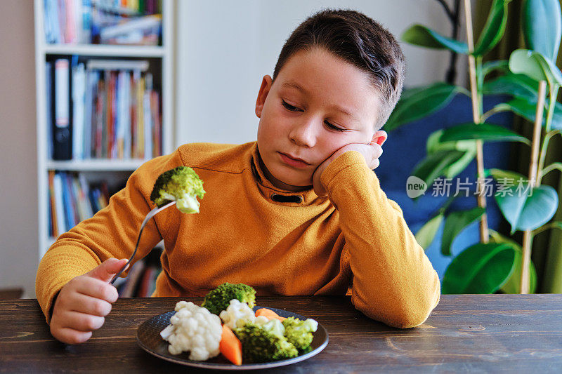 孩子对不得不吃蔬菜很不高兴。他的盘子里有许多蔬菜。他讨厌蔬菜。