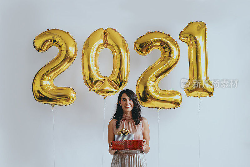新的2021快乐!一个快乐的女人站在新年的气球下拿着礼物(看着相机)