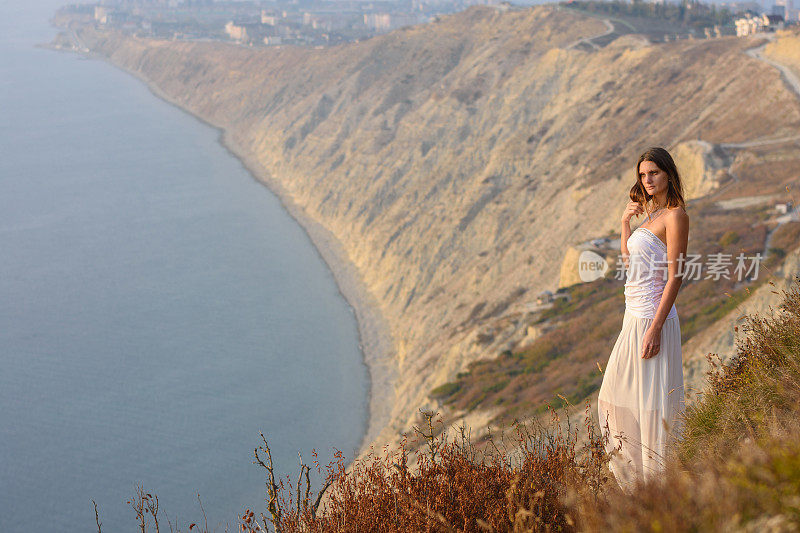一位穿着白色衣服、身材苗条的美丽女孩站在山上欣赏美丽的日落