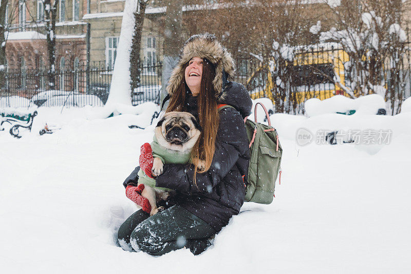 快乐的年轻女子背包享受第一雪在公园散步与小可爱的狗