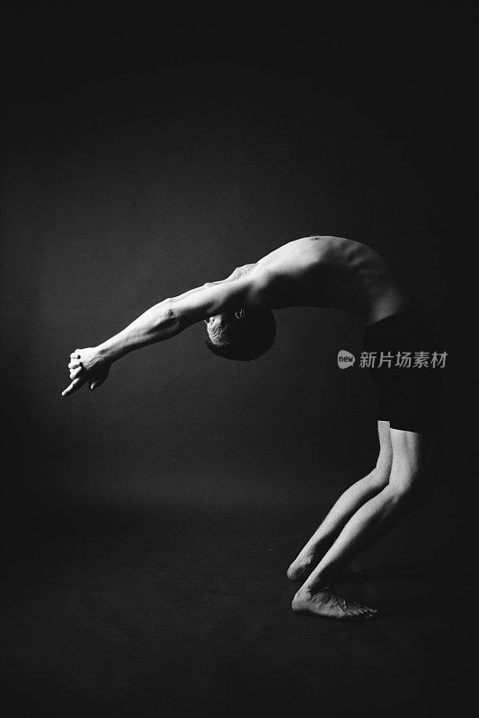 瑜伽锻炼。男子在黑暗的背景下做瑜伽体式。时尚的运动摄影工作室。黑与白，暗与模糊摄影