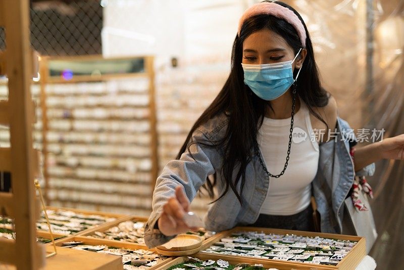 在泰国曼谷当地的夜市，一名戴着防护面膜的女性独自购物