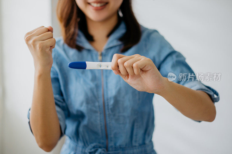 亚洲妇女微笑着拿着验孕棒，结果呈阳性