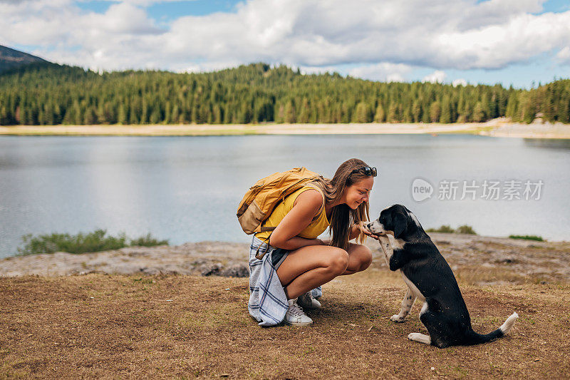 这位千禧一代的女性蹲下来，向走近她的狗狗打招呼。一个女人的手握着狗的爪子。