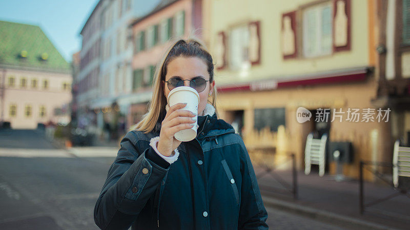 一名年轻女子在科尔马市边喝咖啡边散步。