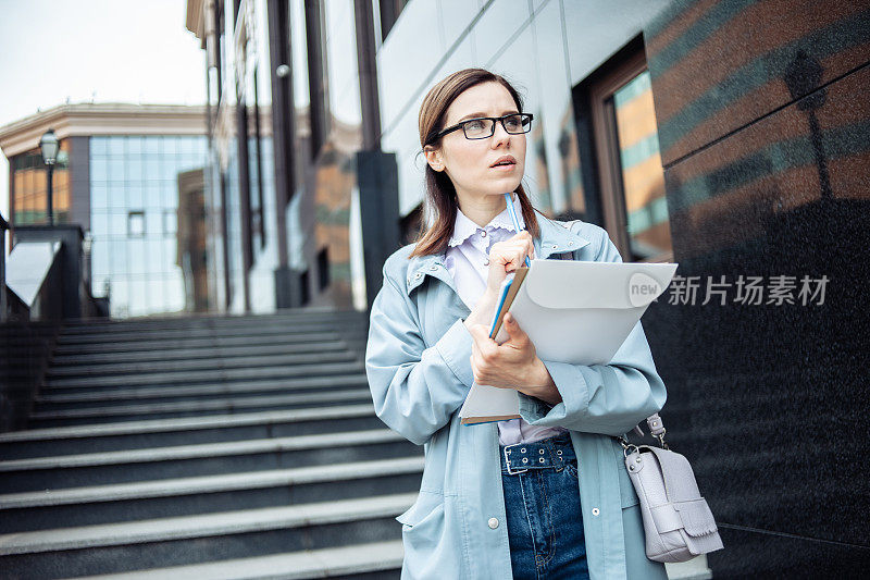 可爱的年轻女商人，戴着眼镜，在城市里装着文件夹。生活方式