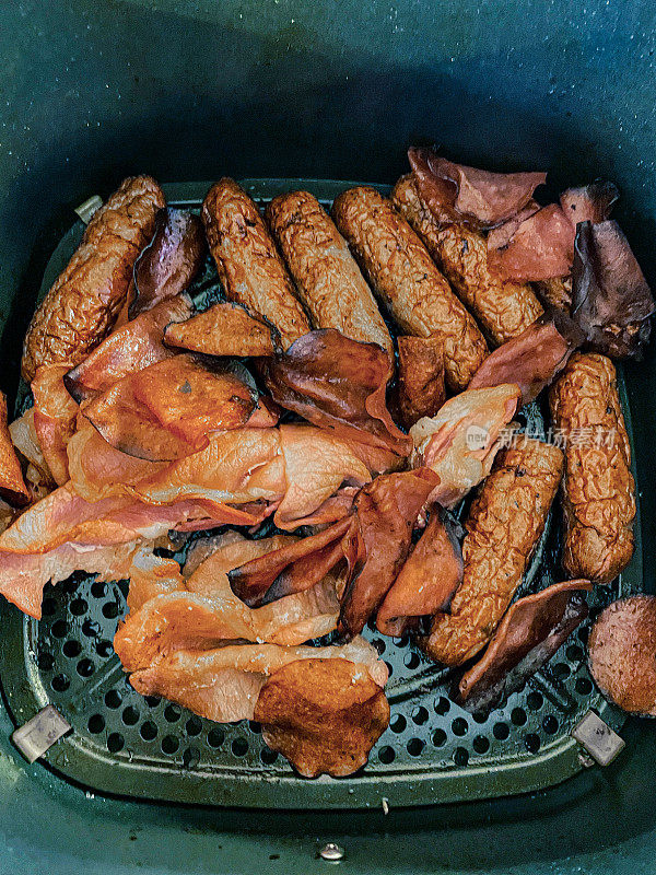 褐色的猪肉香肠和熏肉片在空气炸锅中烹饪，比平底锅烹饪更健康，视野更高