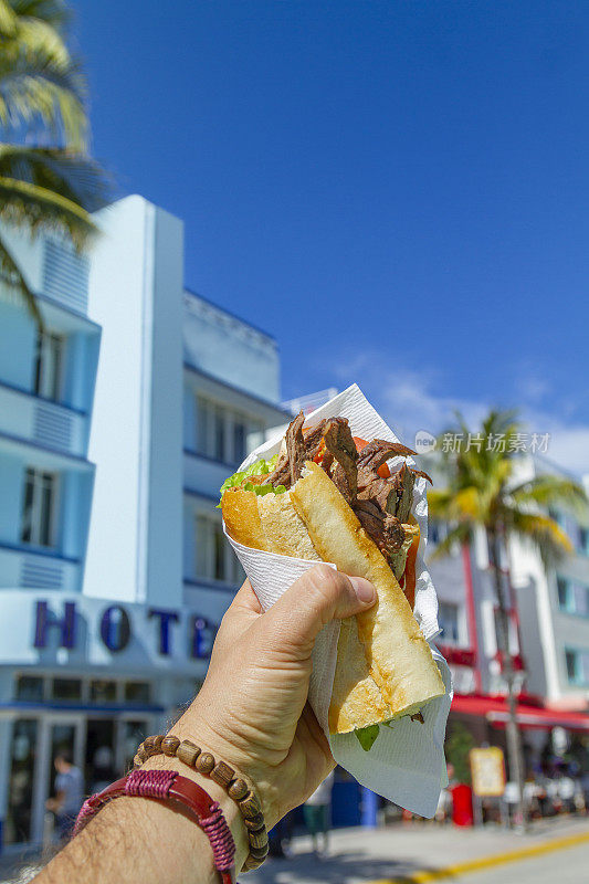 一个年轻的旅行男性享受他的假期，吃着古巴三明治在海洋大道前，南海滩，迈阿密，迈阿密，南佛罗里达，美国。
