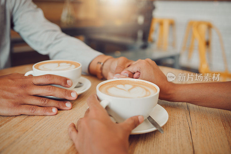 在咖啡馆里，一对相爱的年轻情侣手牵手，桌上放着两杯咖啡。男女在餐厅约会时手拿热卡布奇诺或意式浓缩咖啡