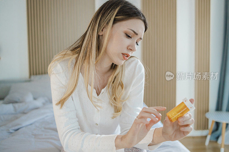 悲伤的年轻女子坐在床上，手里拿着一瓶药